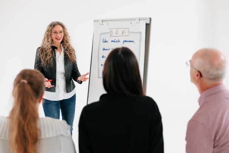 Susanne Rohrbeck vor eine Flipchart stehend im Gespräch und interaktiv mit 3 Zuhörern